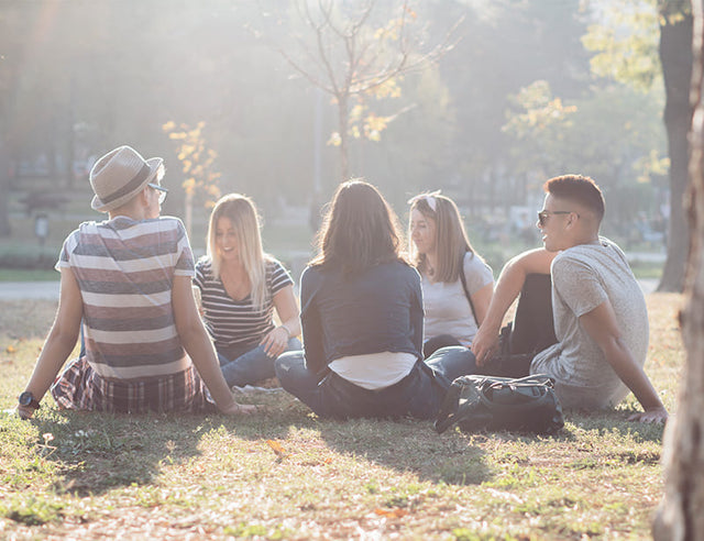 Eine Gruppe junger Menschen in einem Stadtpark; sie sitzen zusammen in einem Kreis im Gras.